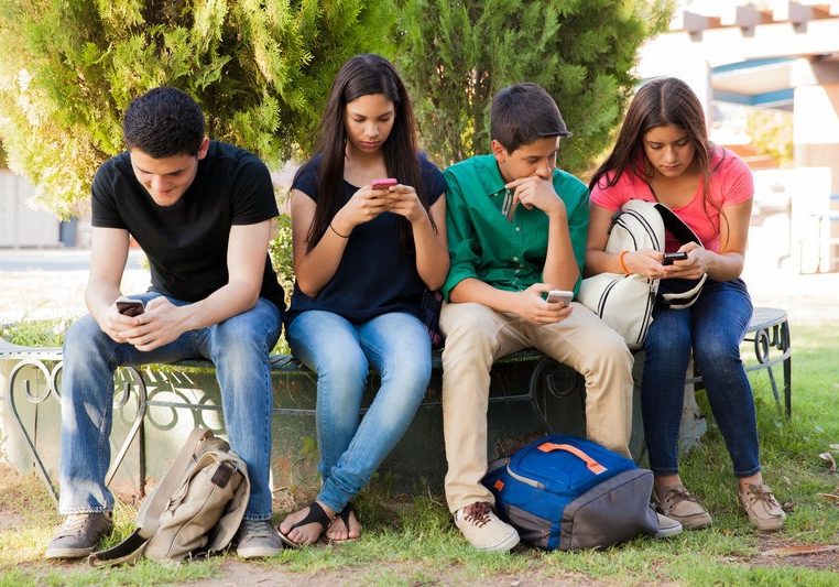 Group of teenage boys and girls ignoring each other while using their cell phones at school